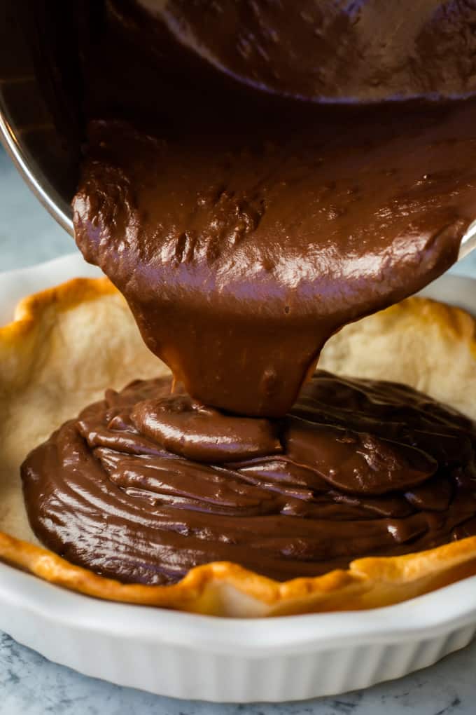 Chocolate pudding being poured in a baked pie crust. 