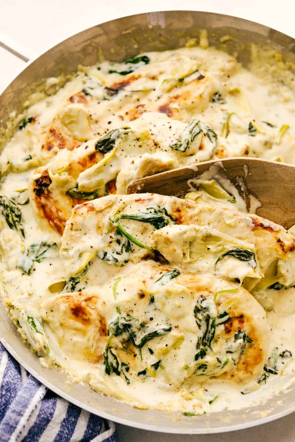 Spooning chicken with spinach artichoke in a creamy sauce.