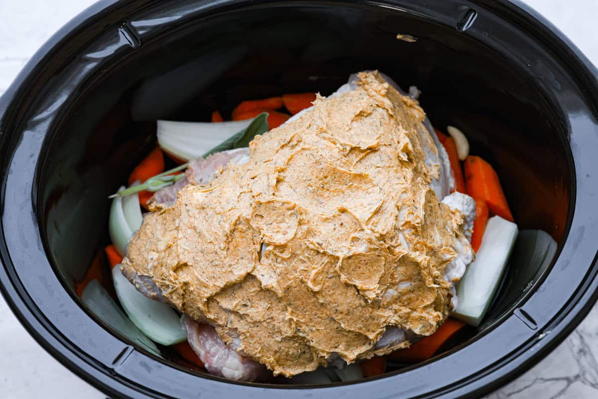 Slow Cooker Turkey Breast is the perfect way to get tender, juicy turkey with a fraction of the prep but all the flavor. Let the slow cooker do ALL the work! Overhead shot of the turkey breast covered in herbed butter on top of the vegetables in the crock pot.