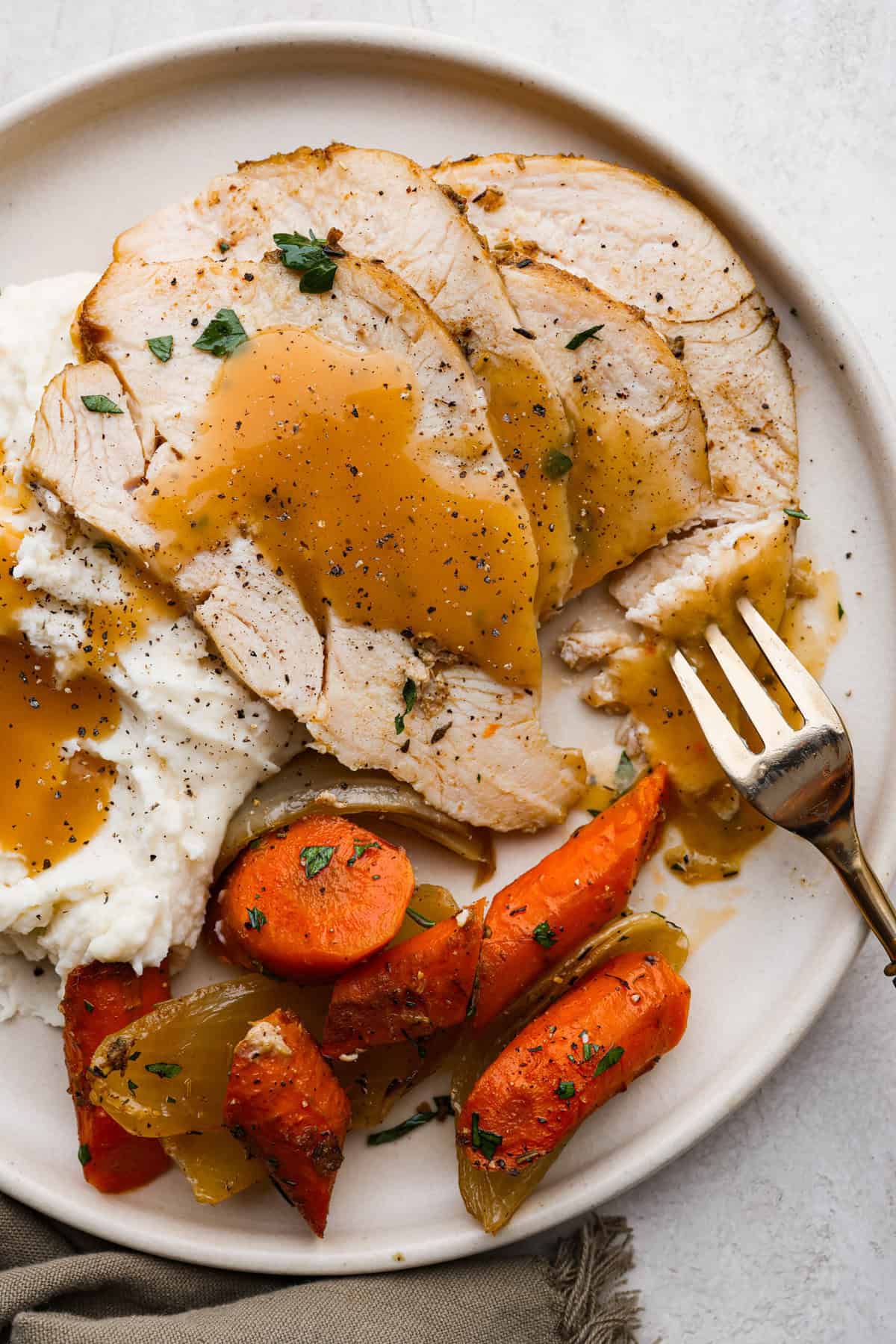 Slow Cooker Turkey Breast is the perfect way to get tender, juicy turkey with a fraction of the prep but all the flavor. Let the slow cooker do ALL the work! Overhead shot of plated slow cooker turkey with gravy and vegetables.