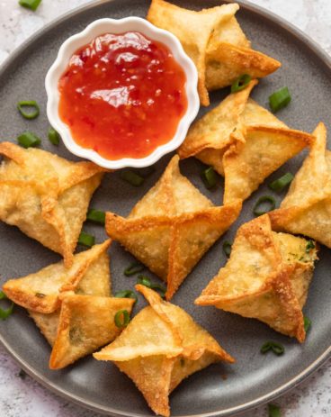 Crab rangoon served on a grey plate with sweet chilli sauce on the side