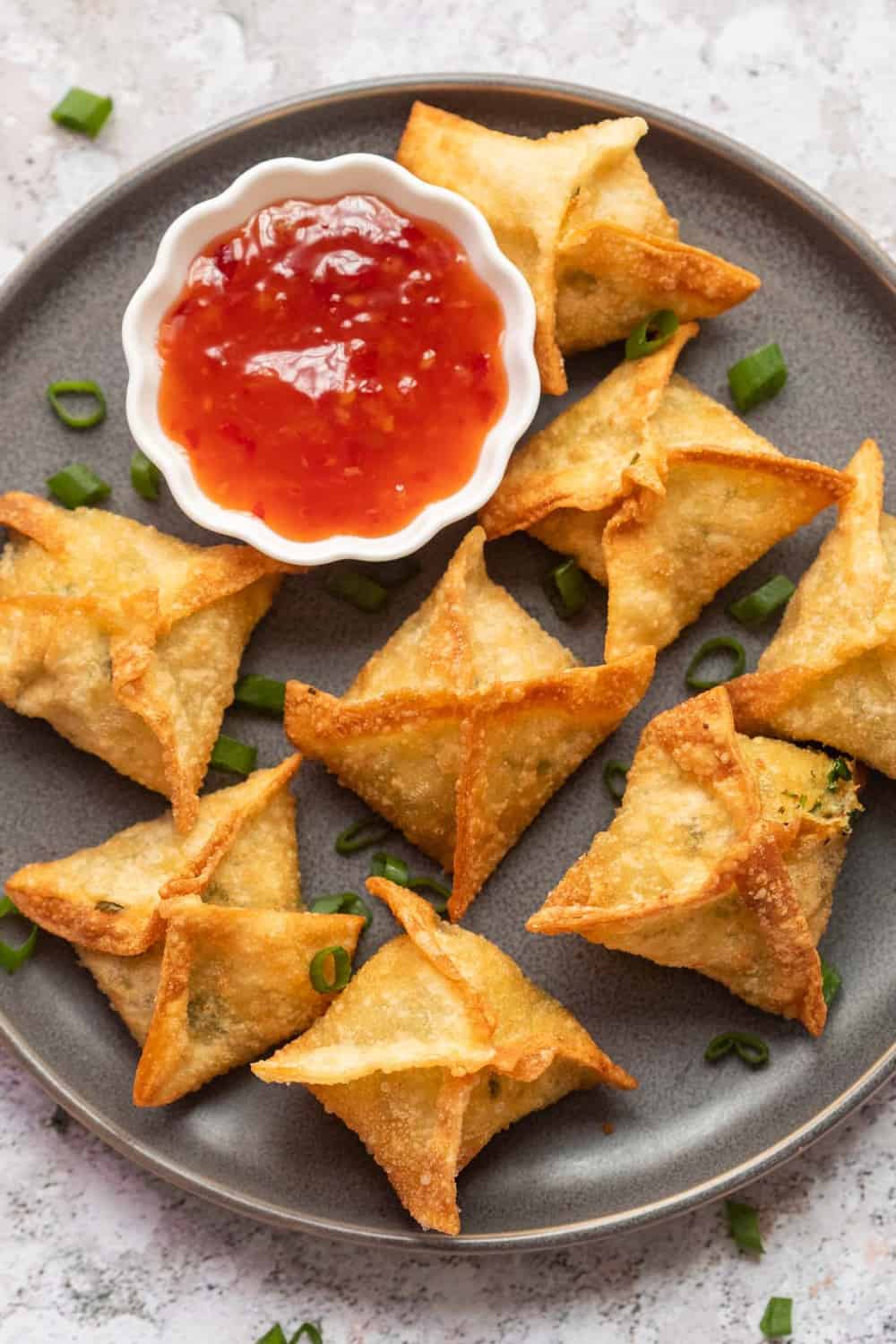 Crab rangoon served on a grey plate with sweet chilli sauce on the side