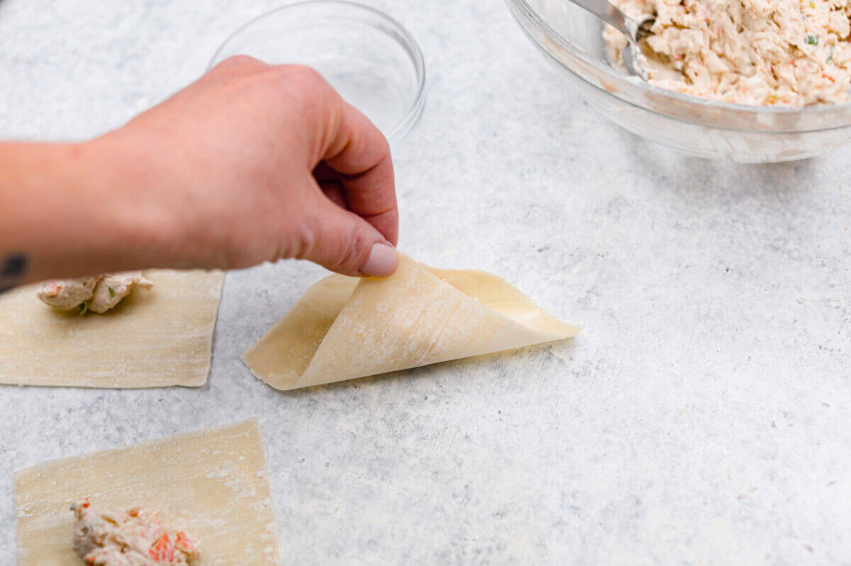 Angle shot of someone pinching two corners of the wonton paper together. 