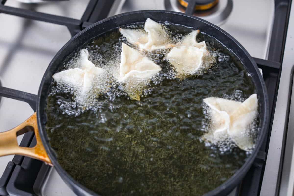 Overhead shot of sealed crab rangoon in oil frying. 