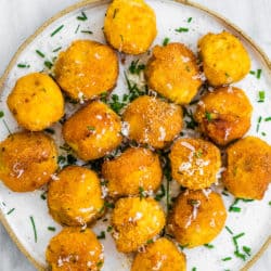 Mashed potato balls on a plate with chives sprinkled on top.