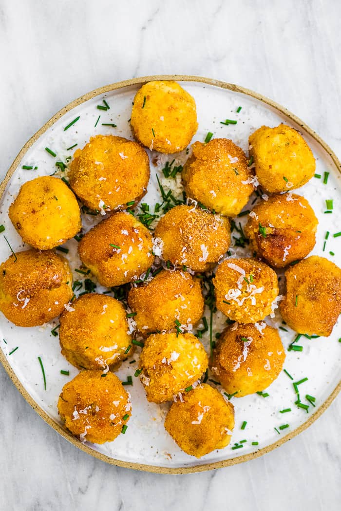 Mashed potato balls on a plate with chives sprinkled on top.