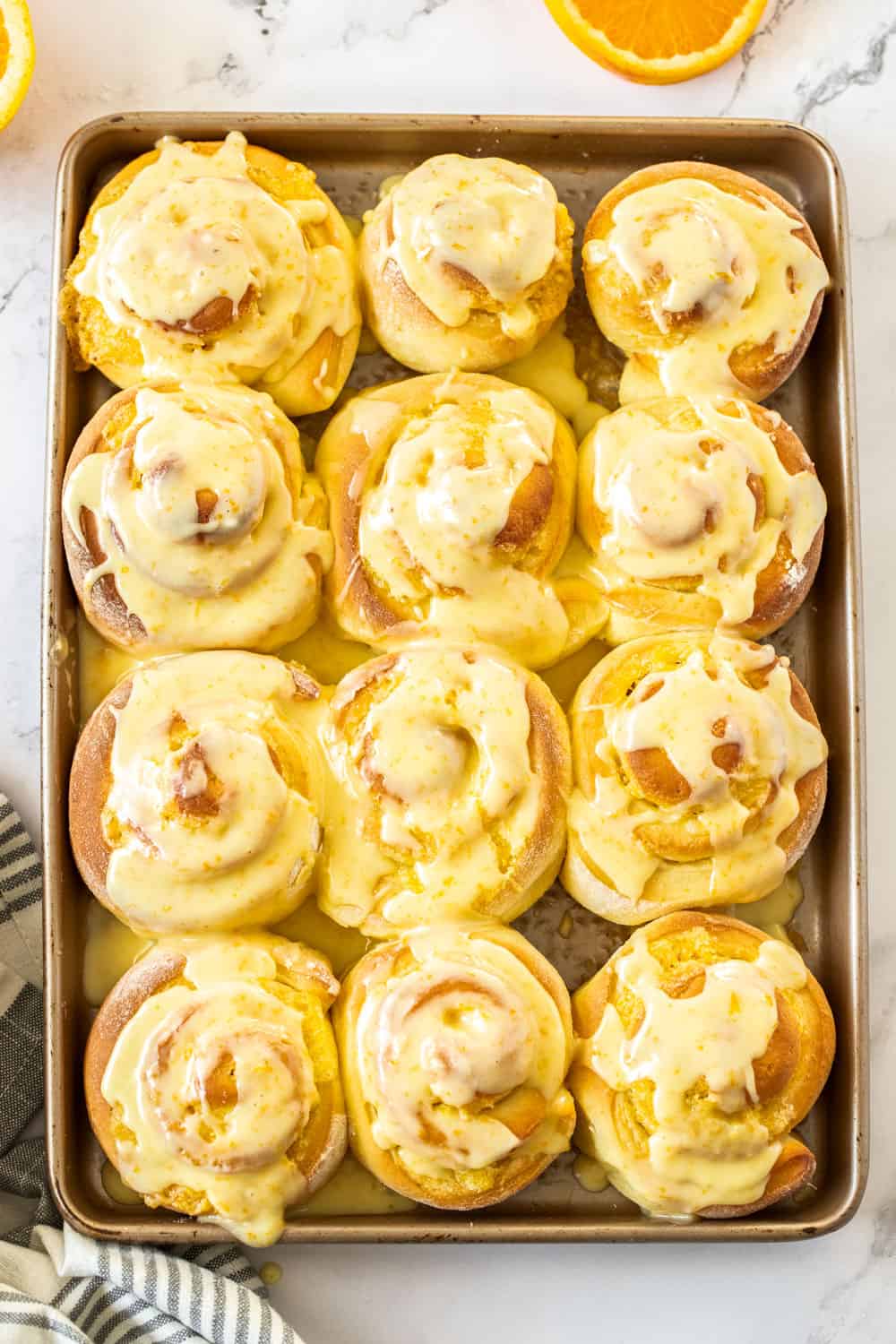 12 orange rolls on a gold baking tray covered in orange icing