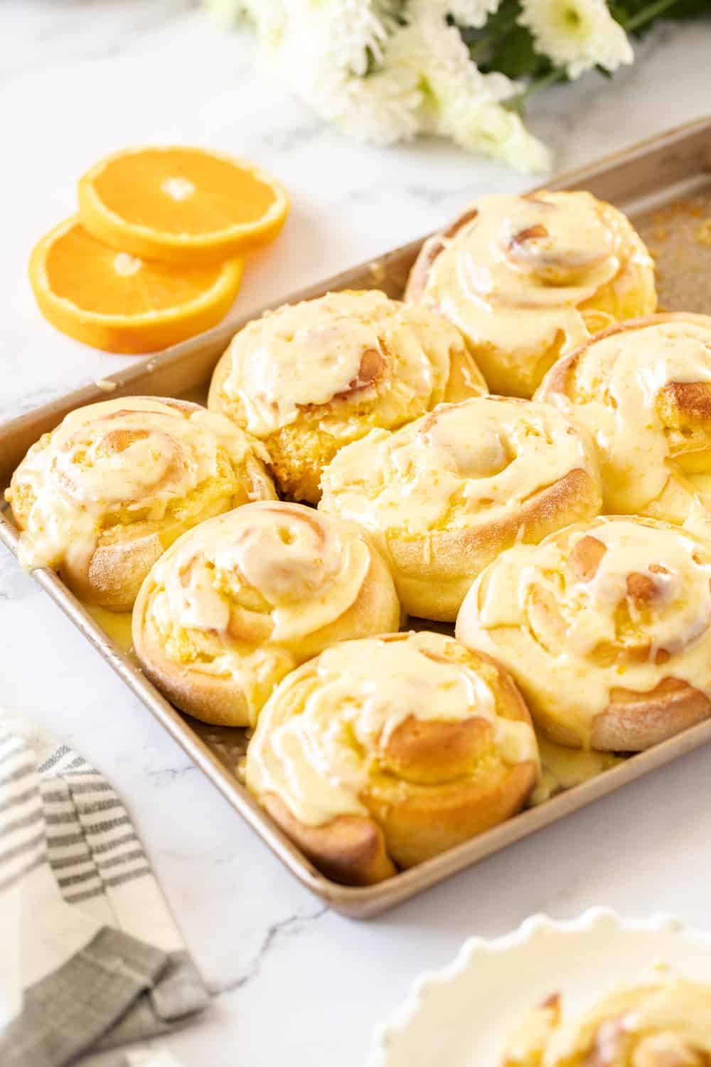 8 orange rolls on a gold baking tray with slices of orange in the background
