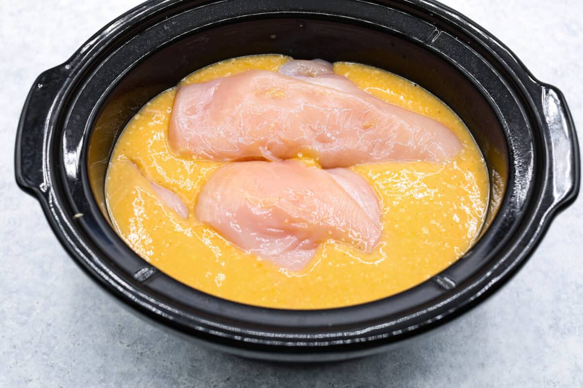 Overhead shot of sauce with chicken breasts on top in crockpot. 