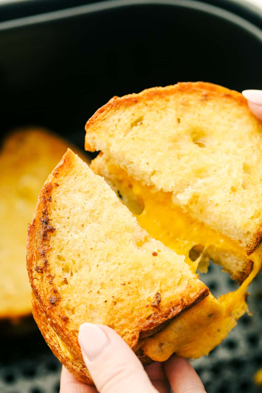 Breaking a grilled cheese from the air fryer with melty cheese inside. 