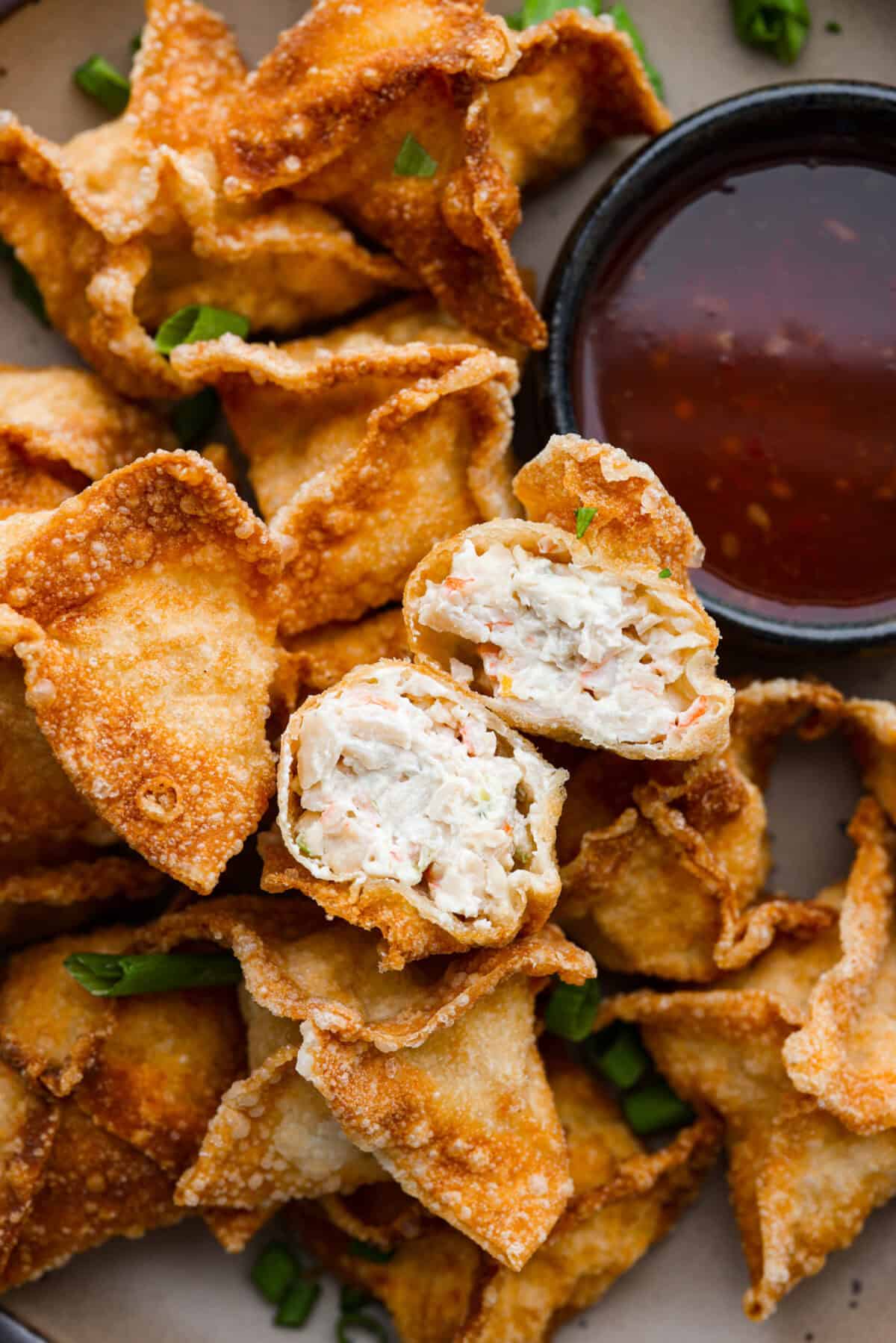 Close up shot of a crab rangoon cut in half over a pile of crab rangoons. 