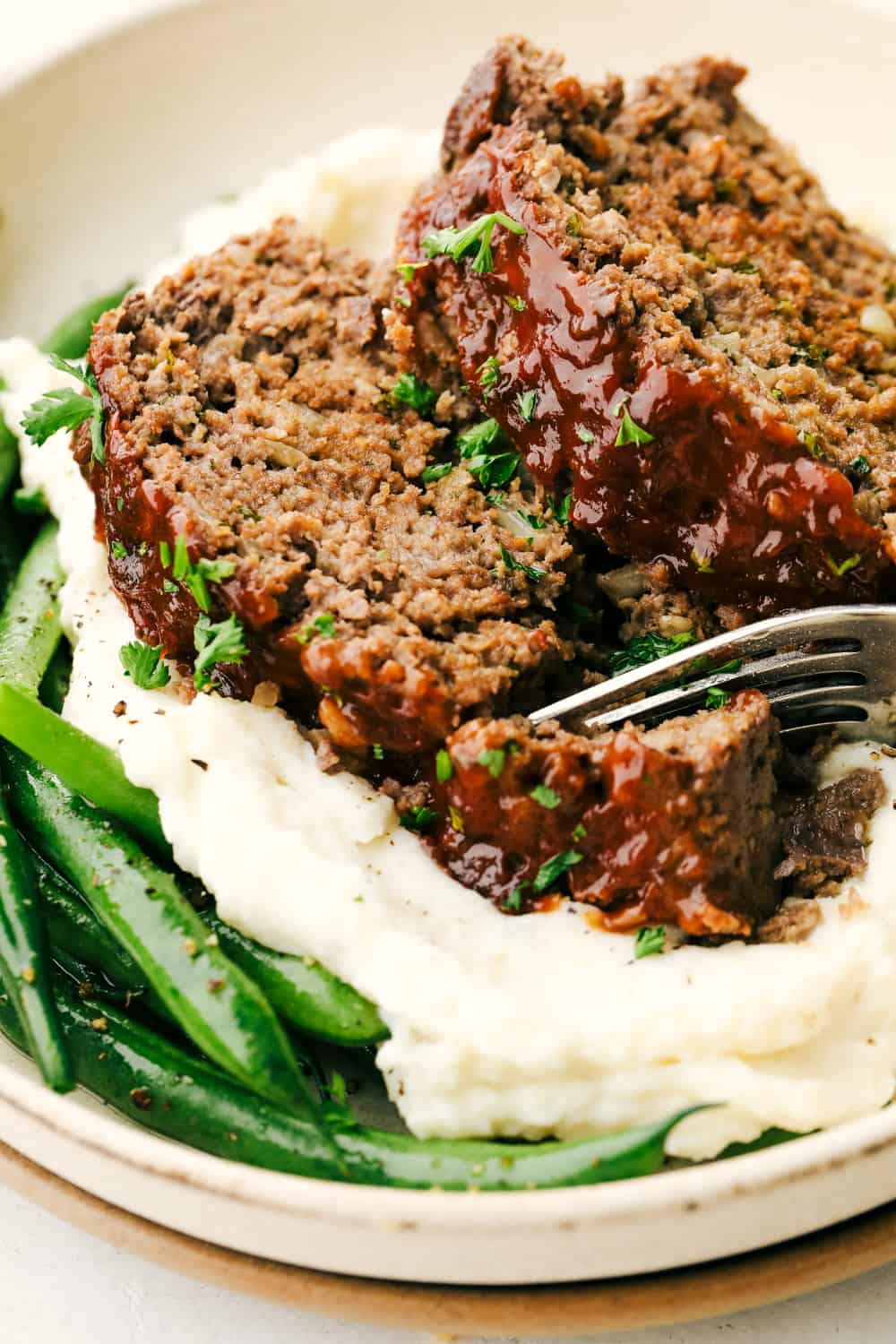 Tender and juicy meatloaf on a bed of mashed potatoes and green beans. 