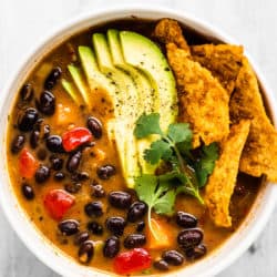 Black bean soup in a white bowl with avocado on top.