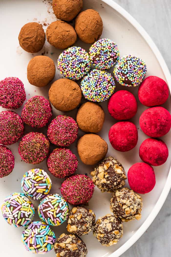 A white platter with multi-colored chocolate truffles.