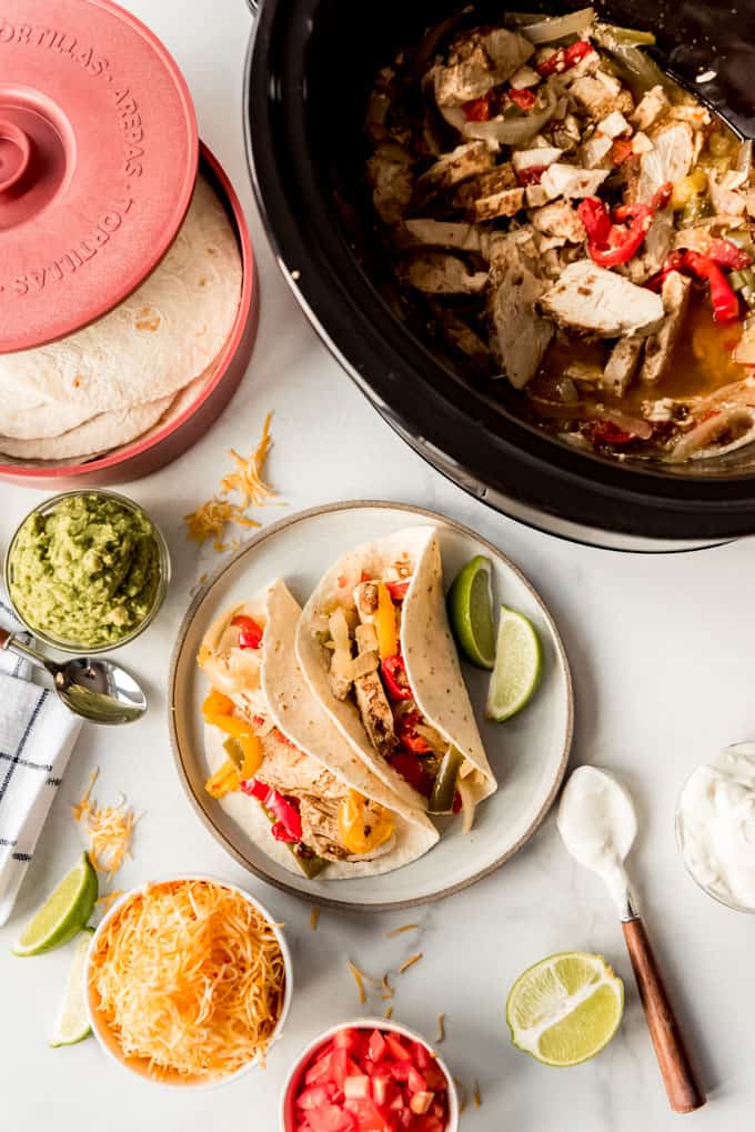 Chicken fajitas with toppings next to a slow cooker.