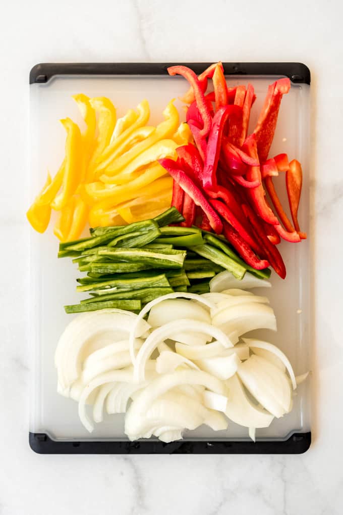 Sliced bell peppers and onions on a cutting board.