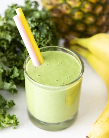 Kale smoothie in a glass surrounded by bananas, kale and pineapple