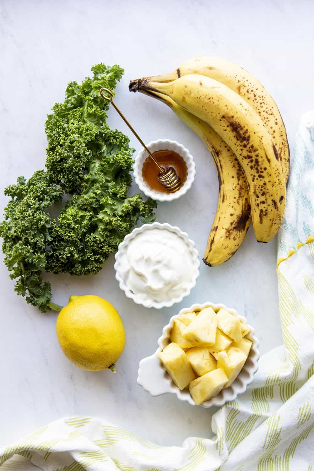 Kale smoothie ingredients on a marble board next to a kitchen towel