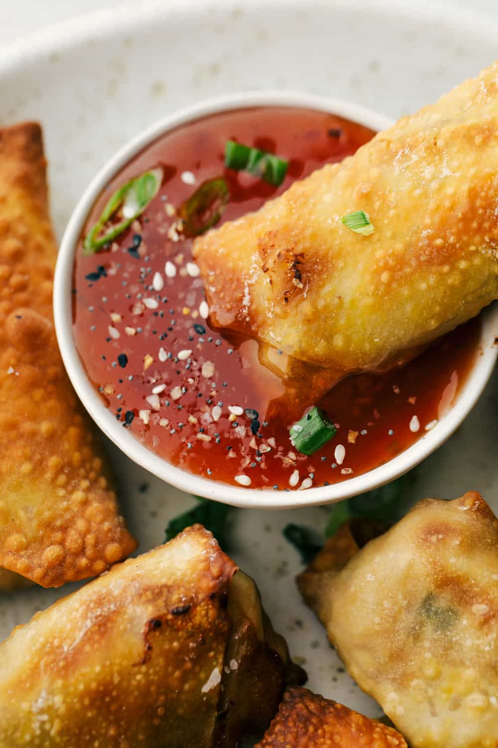 Egg rolls on a plate and one being dipped in sauce. 