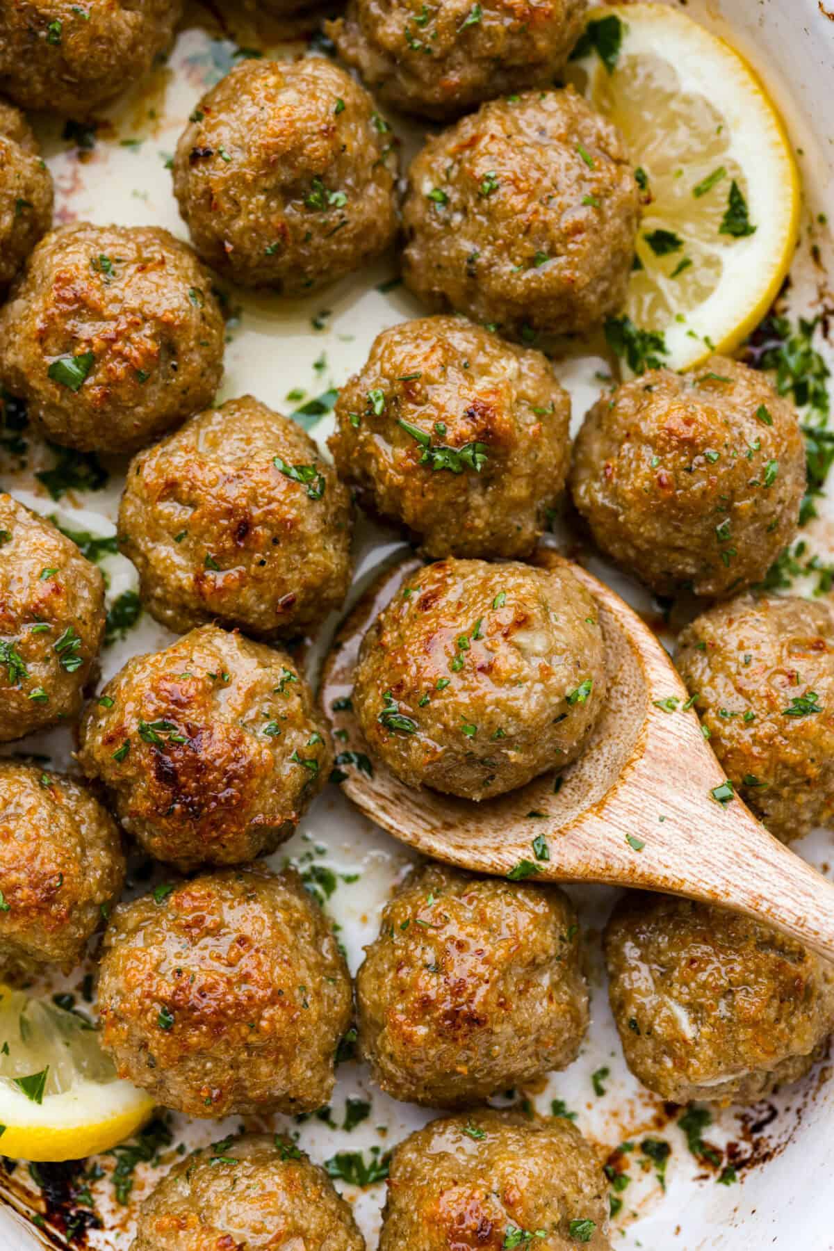 Close view of baked turkey meatballs in a baking dish with a wooden spoon lifting a meatball.