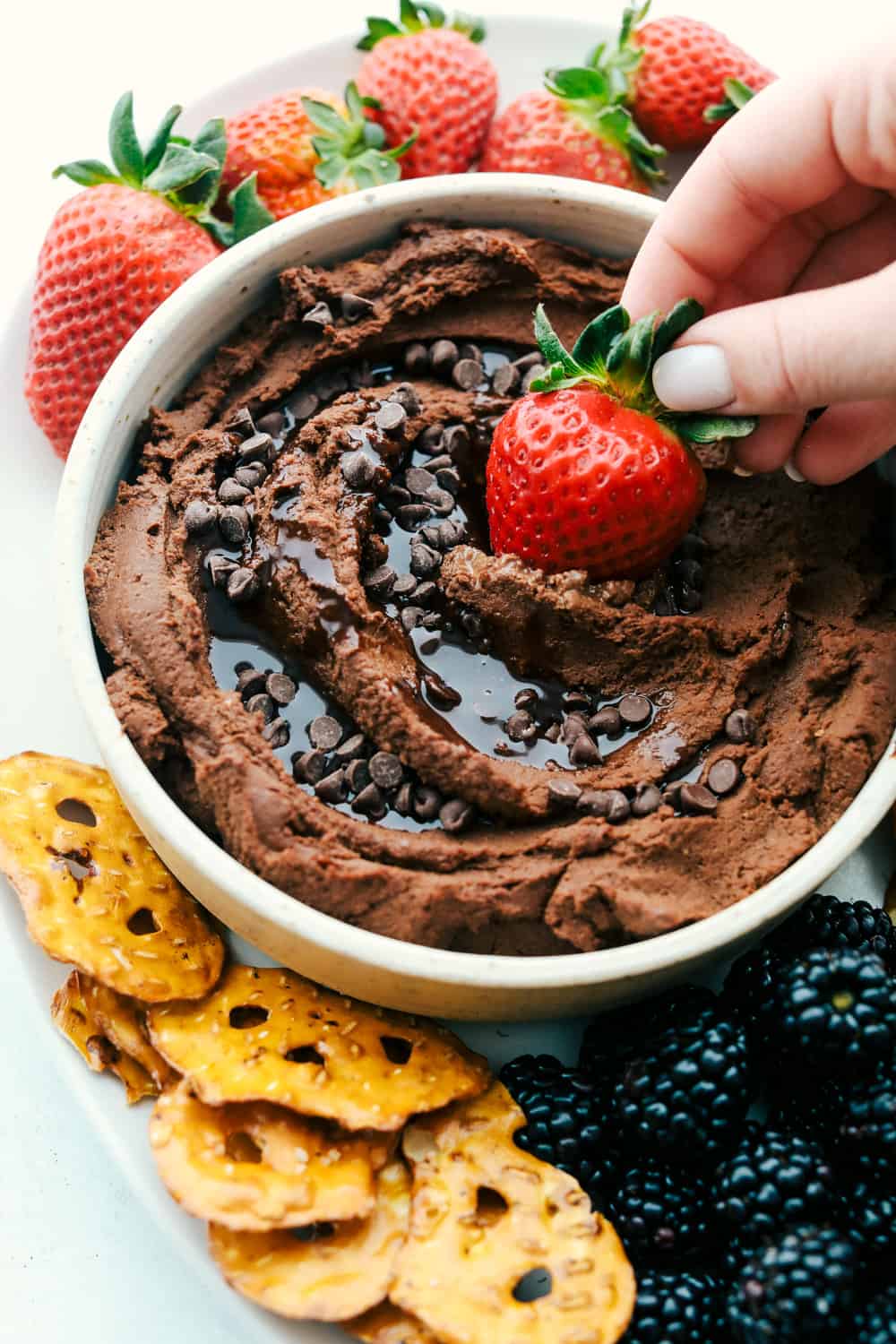 Dipping a strawberry in chocolate hummus garnished with chocolate chips and syrup. 