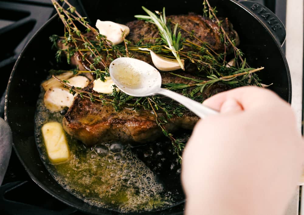 Steak cooking in a black pan with butter and garlic. 
