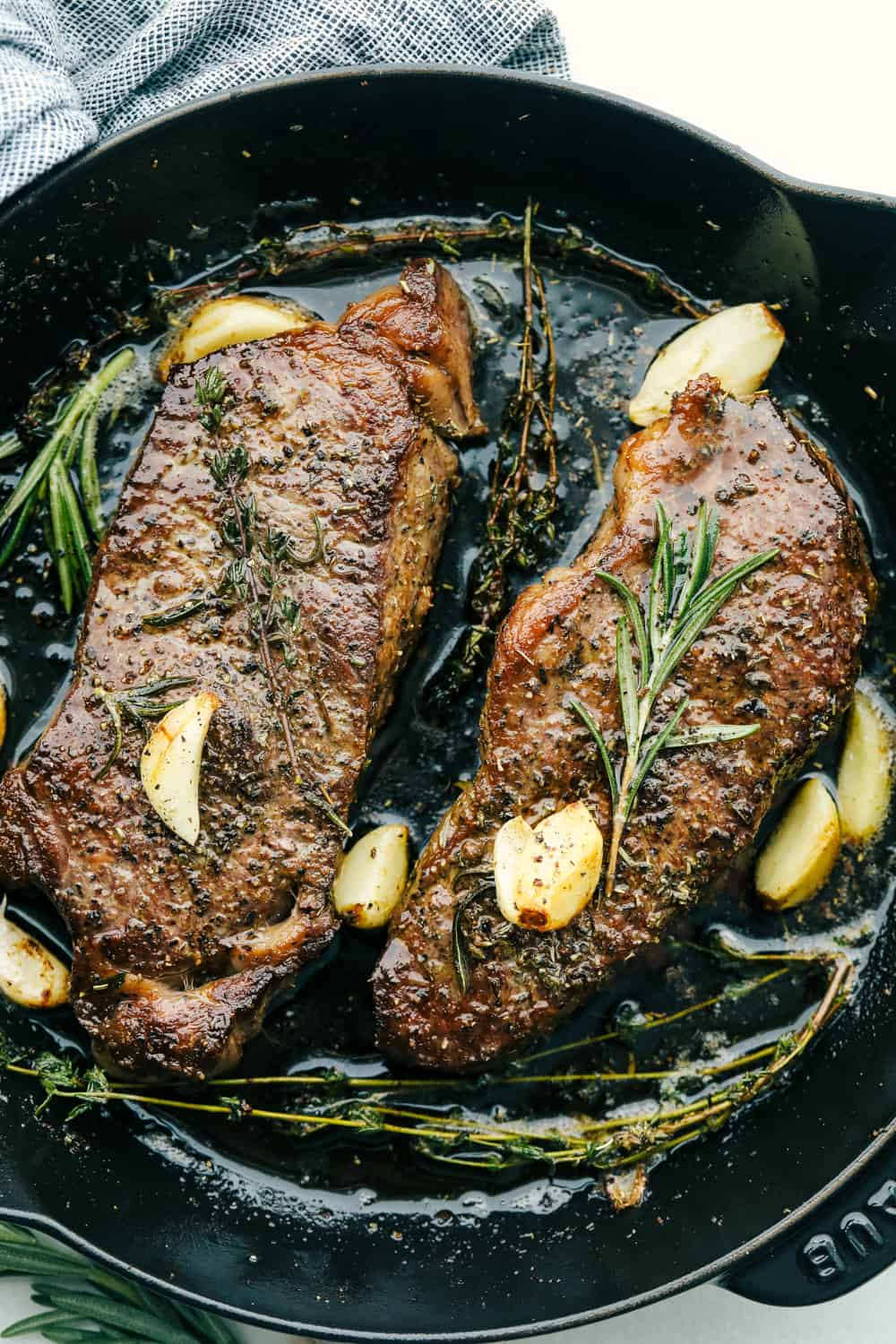 Two steaks in a pan with garlic overtop. 