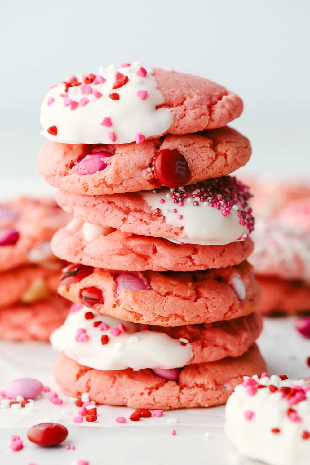 Strawberry cookies with frosting, sprinkles and M&M's in a stack.