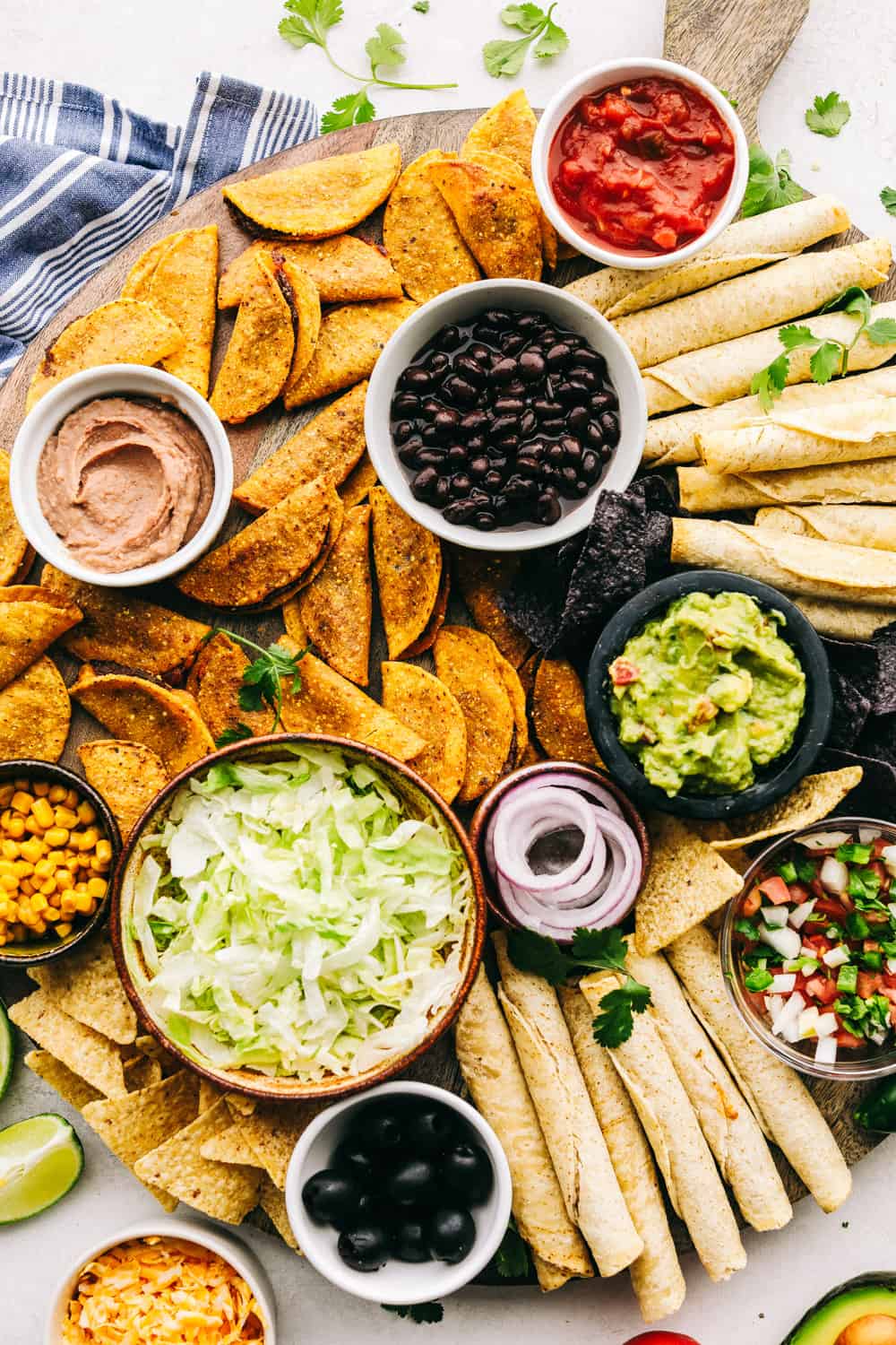 A taco board with dips and salsas with chips and tacos all around. 