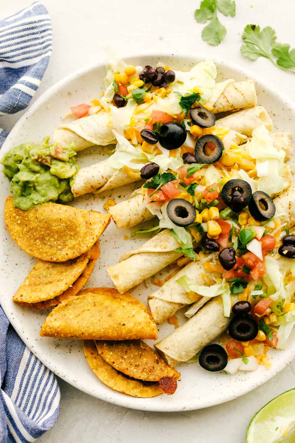 Taquitos smothered with cheese, olives, corn and tomatoes with tacos and guacamole on the side.