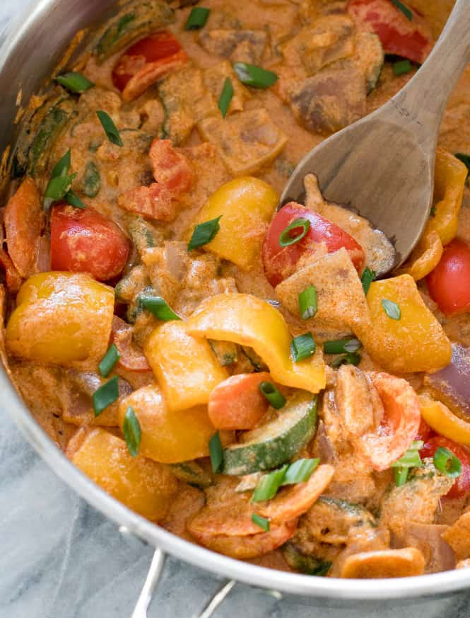 Vegetable curry is in one pot with a wooden spoon in the vegetables. 