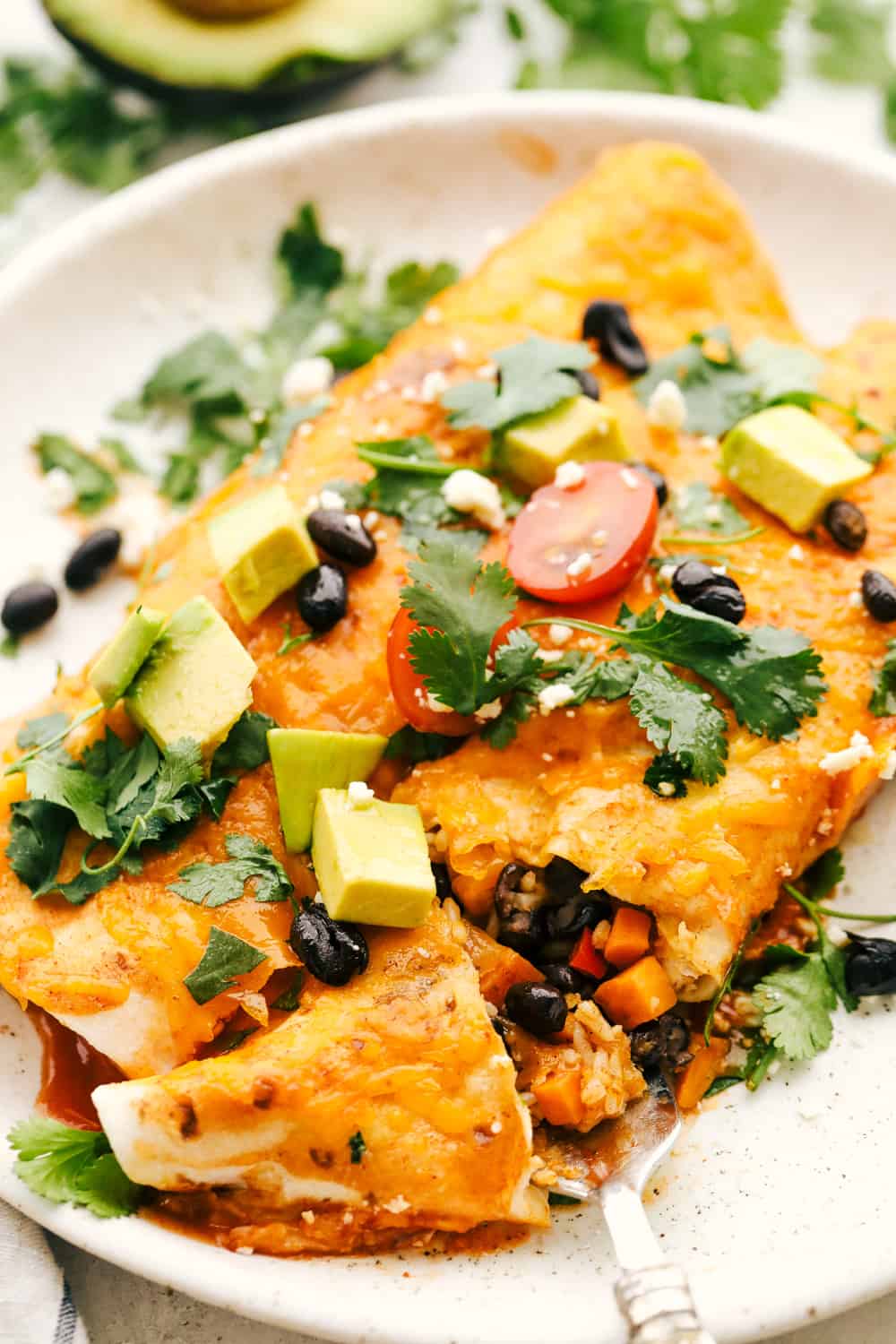Scrumptious black bean and sweet potato enchiladas on a plate with toppings.