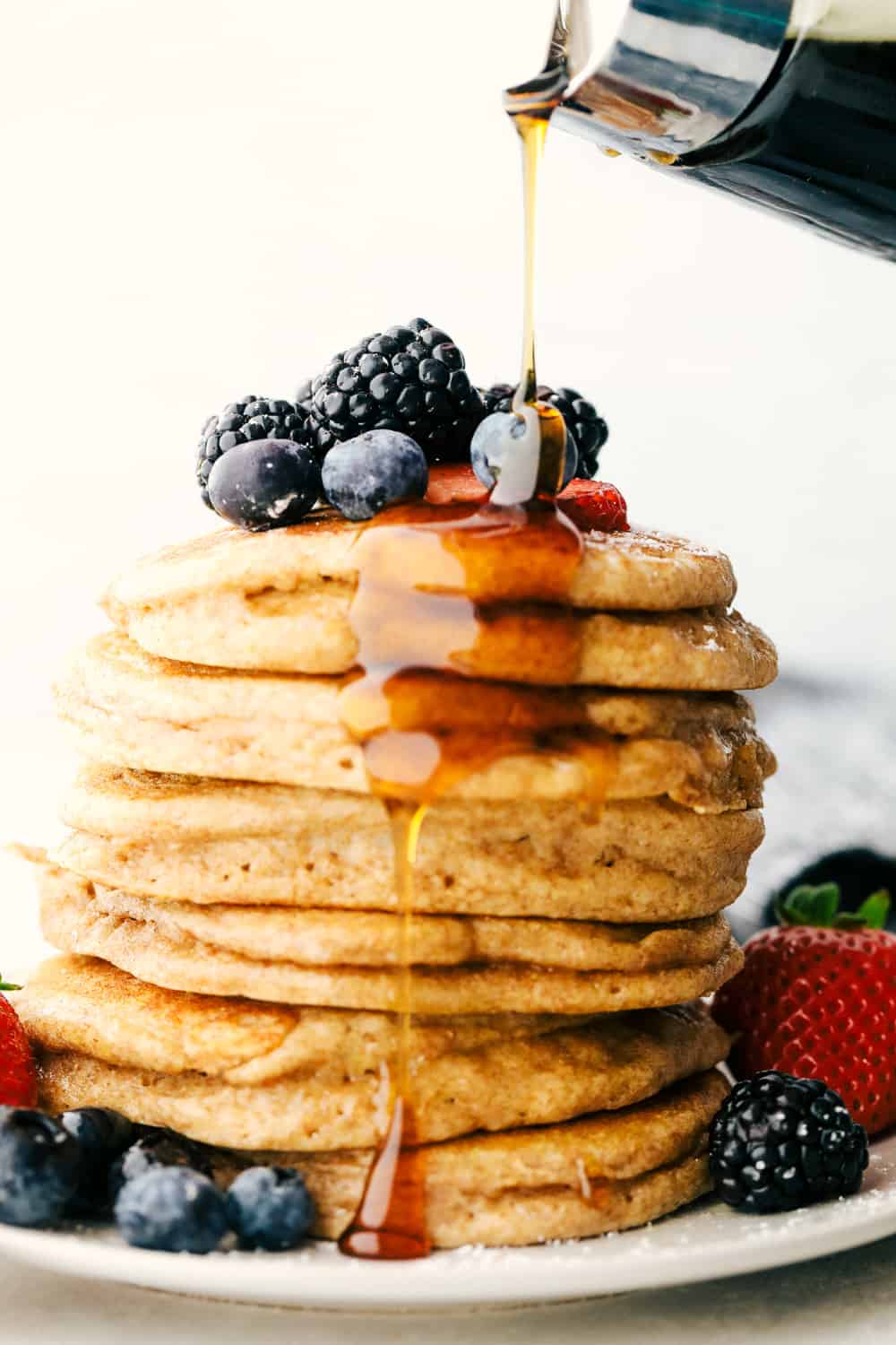 Syrup being poured over a stack of fluffy whole wheat pancakes. 