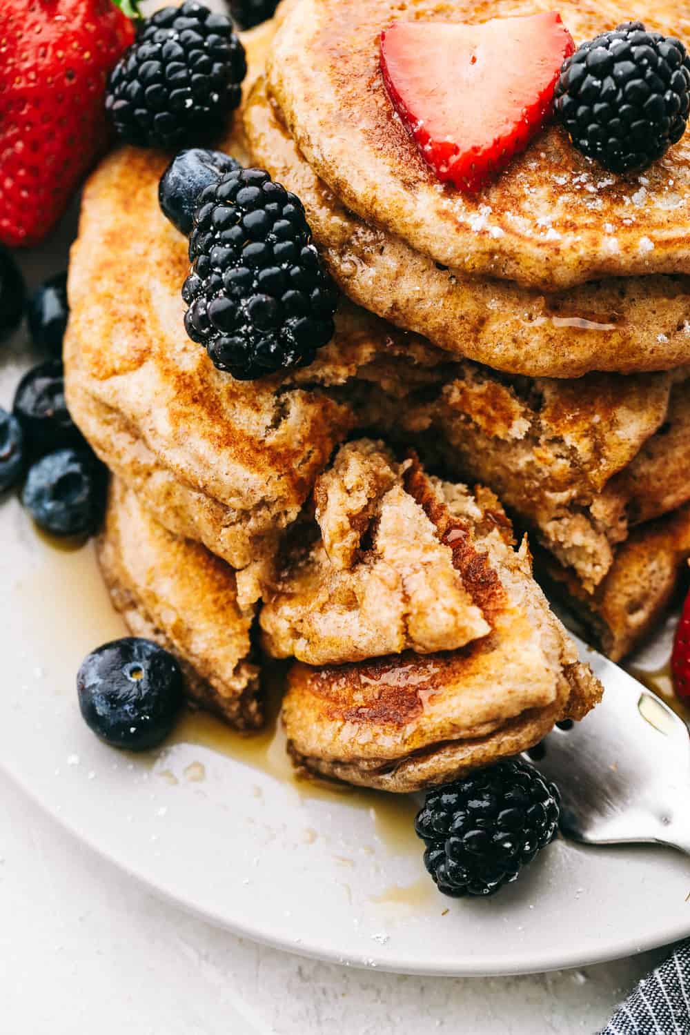 Up close look at whole wheat pancakes cut into with berries and syrup. 