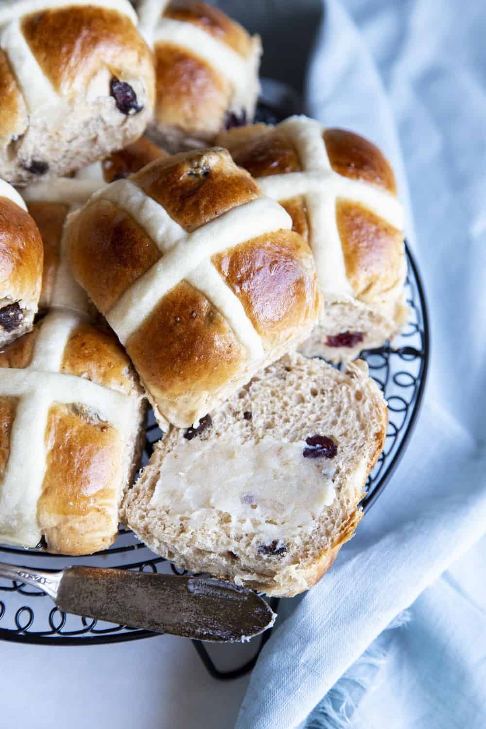 A plate of hot cross buns and one cut open with butter. 