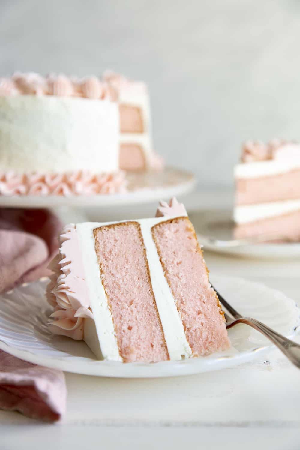 Pink fluffy velvet cake with white frosting and pink swirls on a plate with a fork. 