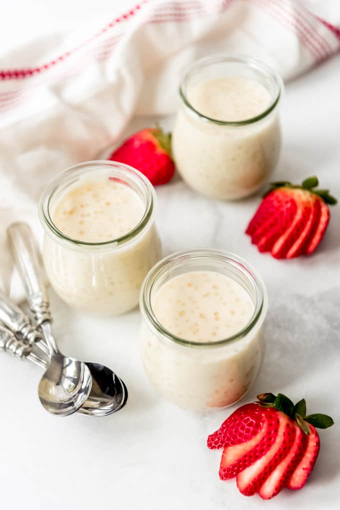 Three glass jars of tapioca pudding next to sliced strawberries.