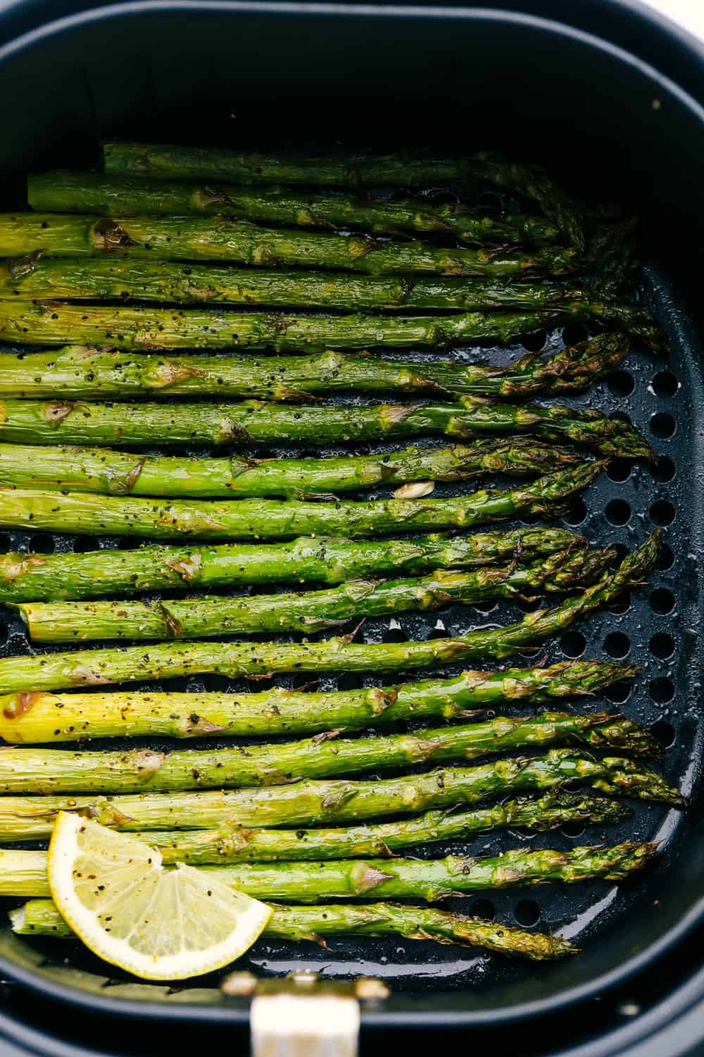 Air fryer roasted asparagus in an air fryer basket with lemon. 