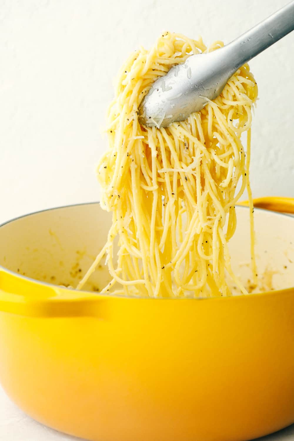 Hot noodles with Pecorino Romano Cheese and seasoning being lifted out of the pot with tongs. 