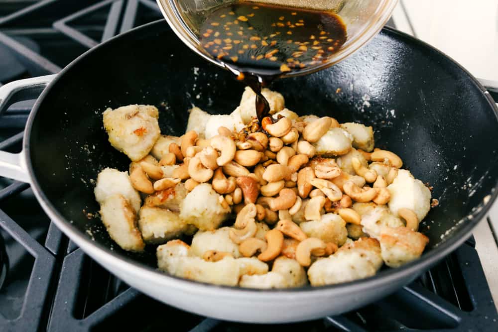 My easy Cashew Chicken recipe skips the breading and frying, but you still get that crispy tender chicken! It all comes together in my flavorful sauce! Someone pouring sauce over cashew mixture in a wok.