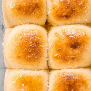 Potato buns in a baking pan with honey butter on top.