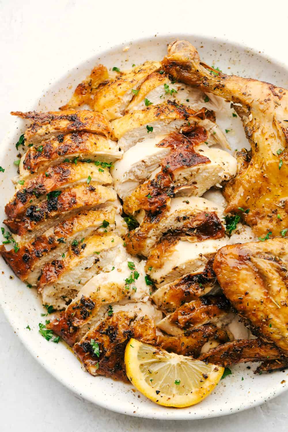 Sliced juicy chicken on a plate with a wedge of lemon.