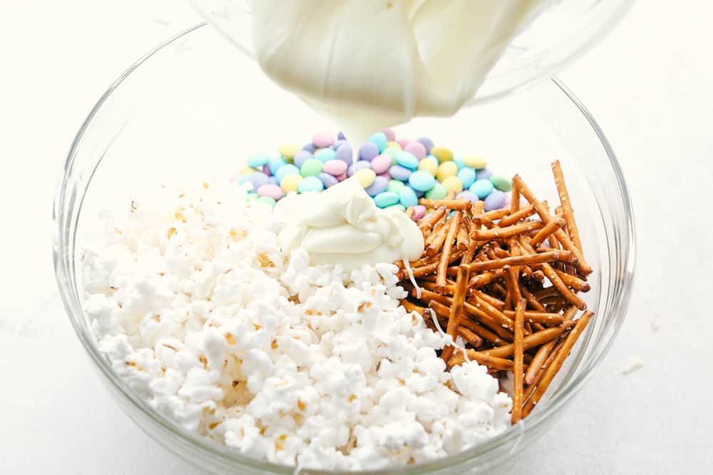 Pouring melted white chocolate over popcorn, M&Ms and pretzels. 