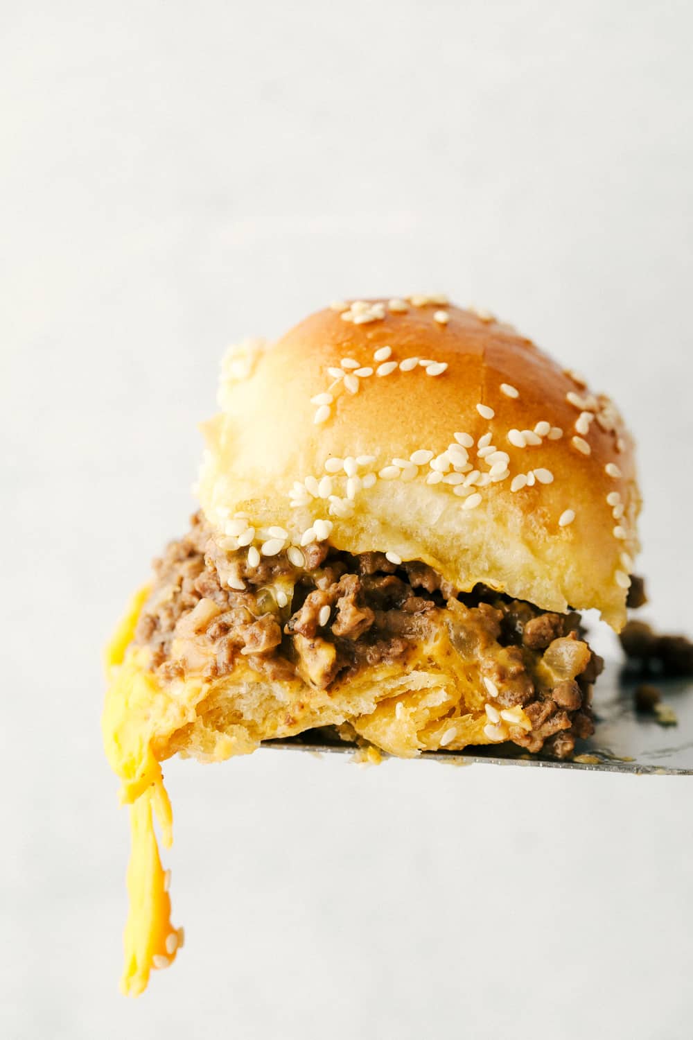 A single slider on a spatula with cheese dripping off. 