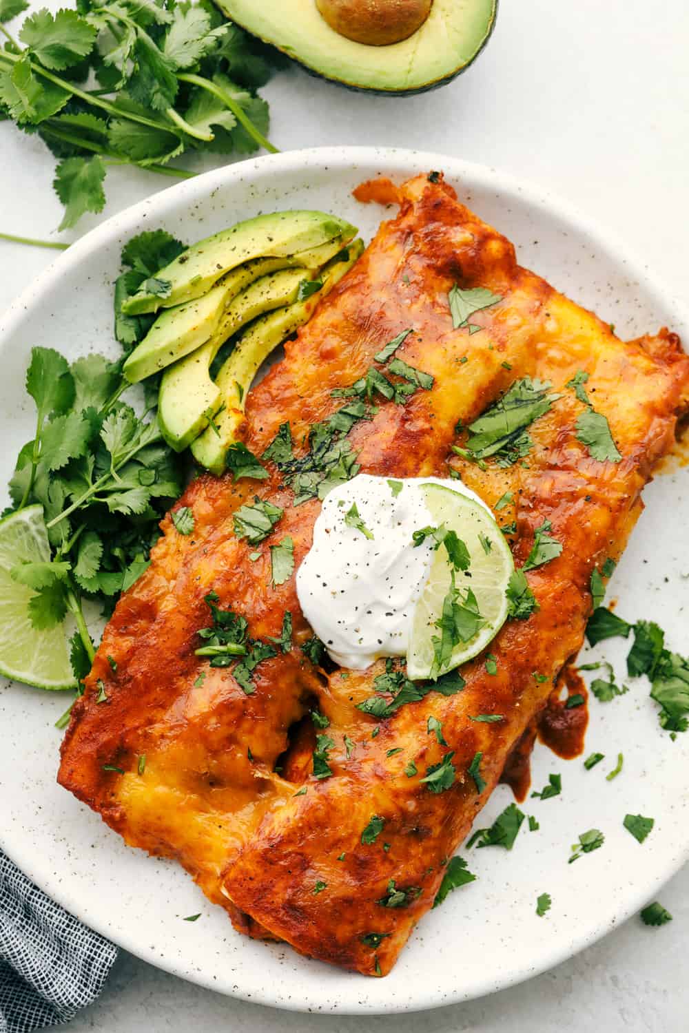 Enchiladas on a plate with sour cream and sliced avocados. 