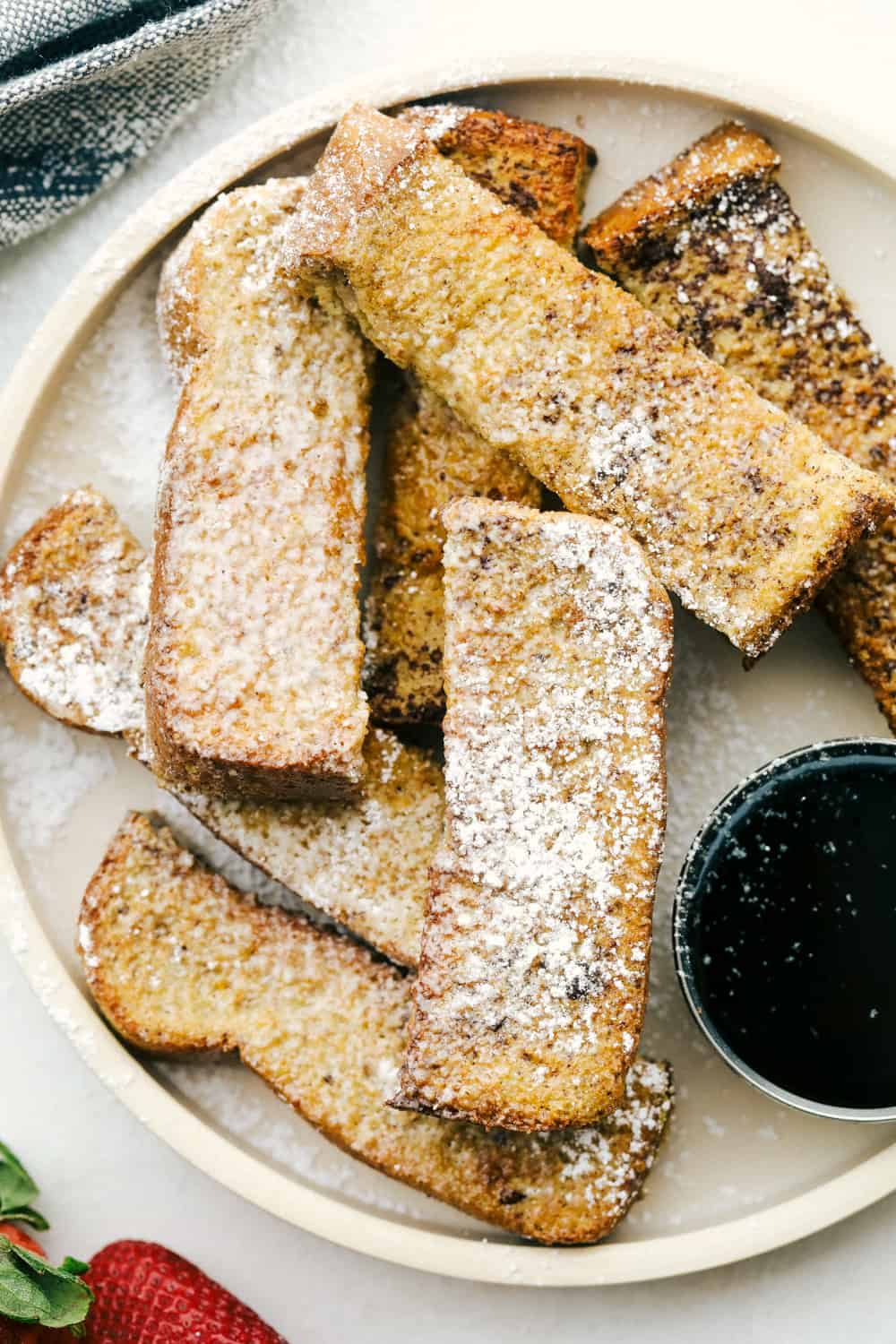 Air fryer french toast sticks layered on a plate with powdered sugar