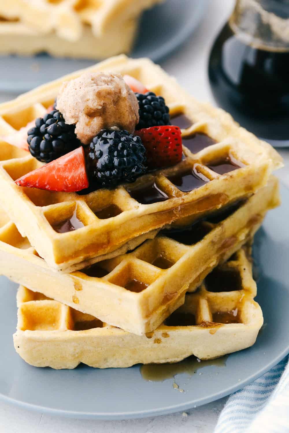 A Stack of fluffy waffles with fruit and syrup on a plate. 