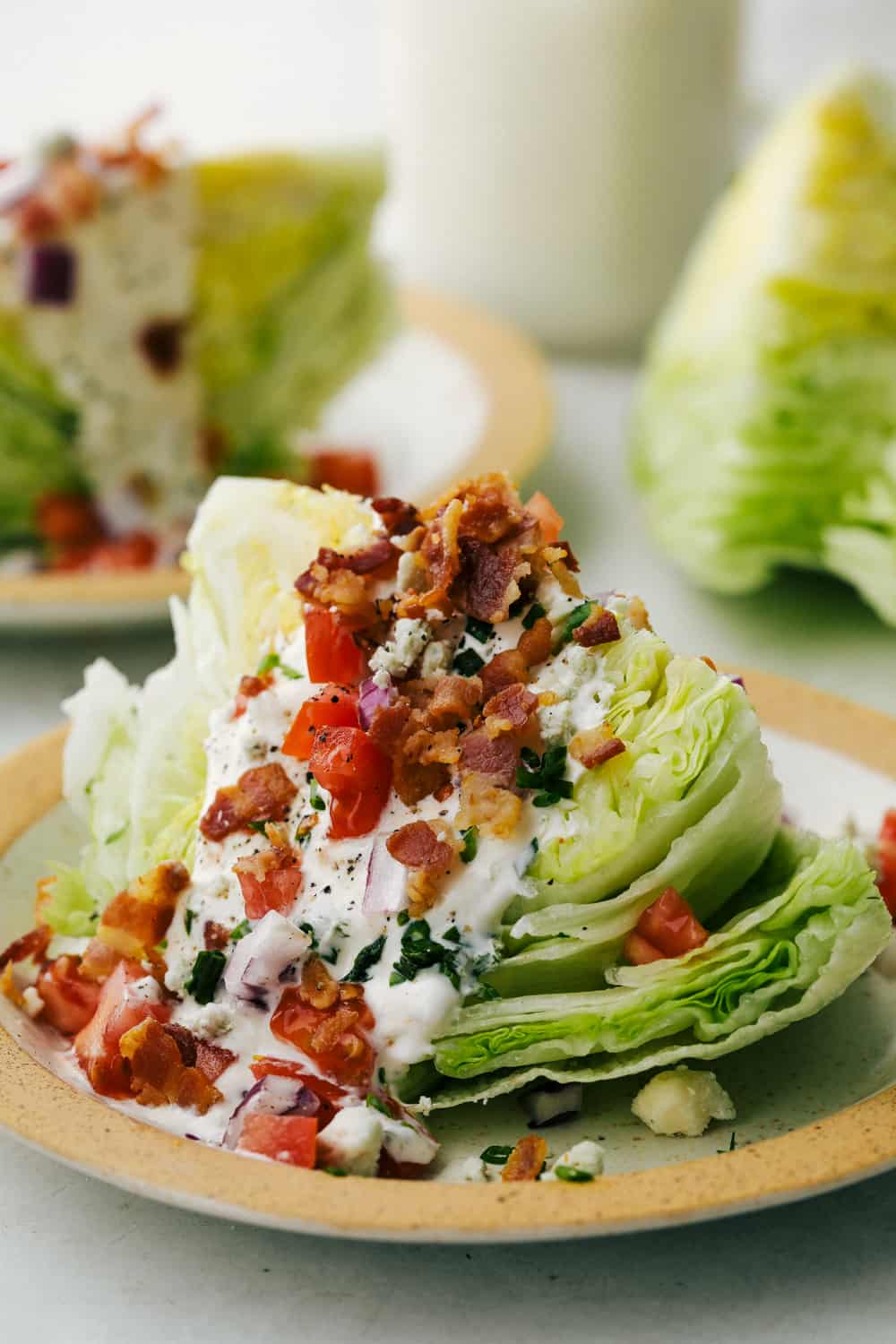 Classic wedge salad topped with tomatoes, bacon and blue cheese dressing on a plate. 