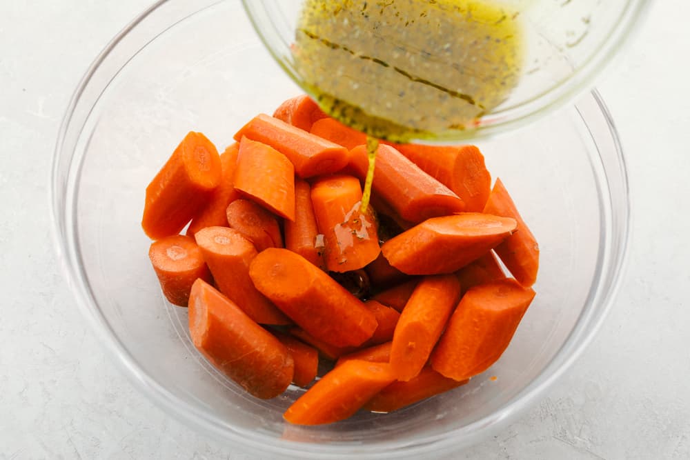 Pouring the seasoning on cut sliced carrots.