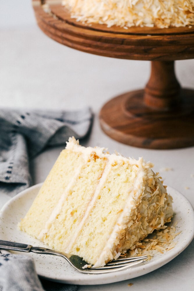 A slice of coconut cake with frosting and toasted coconut on a plate. 